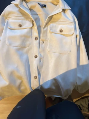 Beige skjorta från SMOG XS - Stilren beige skjorta från SMOG i relaxed fit. Skjortan har två stora bröstfickor med knappar och klassisk krage. Perfekt för en avslappnad och trendig look.