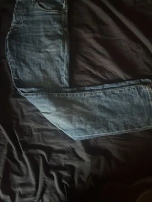 Blå slim fit - Säljer ett par blå jeans med rak passform och klassisk femficksdesign. Jeansen har en snygg tvättad look och är tillverkade i denim. Perfekta för en avslappnad och stilren outfit.