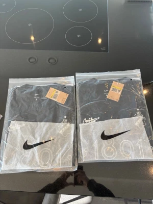 Svart Nike t-shirt med tryck - Svart t-shirt från Nike med vitt tryck och stor Nike-logga framtill. T-shirten har klassisk passform och rund halsringning. Perfekt för en sportig och stilren look.