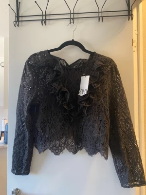 Svart spetsblus med volanger från Zara - Supersnygg svart spetsblus från Zara med långa ärmar och volangdetaljer framtill, helt oanvänd!😍