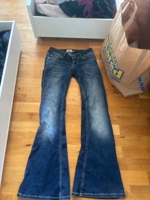 Blå bootcut jeans från 1969 - Säljer ett par blå bootcut jeans från 1969 med snygg slitning framtill. Jeansen har klassisk femficksmodell, låg midja och utsvängda ben. Tillverkade i denim med en cool tvättad look. Perfekta för dig som gillar retrostil och vill ha ett par jeans som sticker ut.