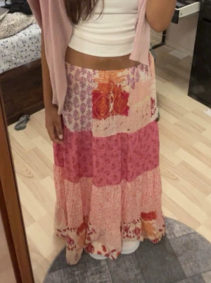 Långkjol i rosa patchworkmönster - Säljer en flowy långkjol i olika rosa och röda nyanser med patchwork och blommigt mönster. Kjolen har bred resår i midjan och är gjord i ett lätt, mjukt material som passar perfekt till sommaren. Superskön och bohemisk vibe! Perfekt till sommaren! 