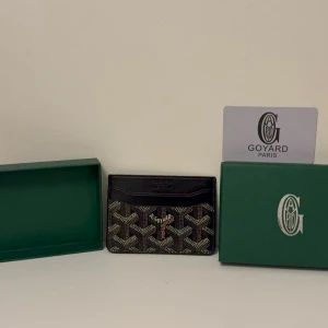 Svart kortfodral  - Säljer ett stilrent svart kortfodral  med det klassiska mönstret i vitt, brunt och beige. Fodralet har flera kortfack och är tillverkat i canvas med läderdetaljer. Perfekt för dig som vill ha en exklusiv accessoar i fickan.