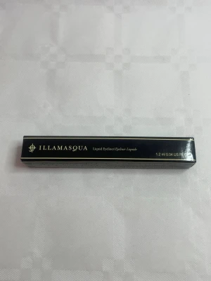 Illamasqua Liquid Eyeliner svart - Illamasqua Liquid Eyeliner i svart nyans, 1,2 ml. Kommer i en elegant svart förpackning med guldtext. Perfekt för att skapa skarpa och definierade linjer runt ögonen. Flytande formula som ger intensiv färg och lång hållbarhet.