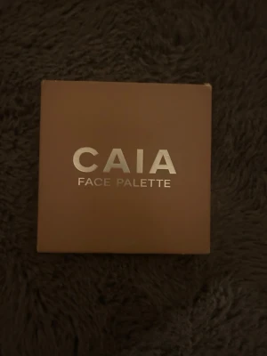 CAIA Face Palette brun - Säljer en CAIA Face Palette i en stilren brun fyrkantig förpackning med silvrig text. Perfekt för att skapa en fräsch bas och highlighta ansiktet. Paletten är kompakt och enkel att ta med i väskan.