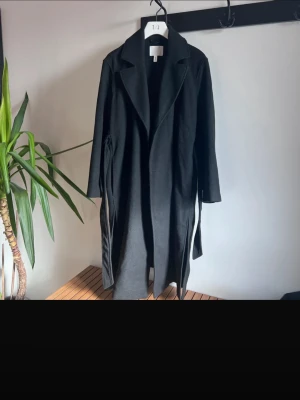 Svart lång kappa med skärp - Säljer min jättefina långa kappa. Knappt använd så väldigt bra skick. Storlek S