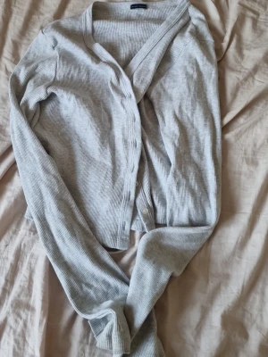 Ljusgrå ribbad kofta Brandy Melville - Säljer en ljusgrå ribbad kofta från Brandy Melville. Koftan har långa ärmar, v-ringad hals och knäppning framtill med små knappar. Materialet är mjukt och stretchigt, perfekt för lager på lager och en chill look.