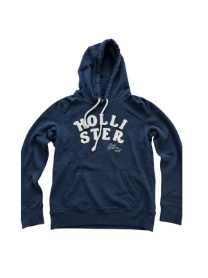 Blå Hollister hoodie med broderad logga - Blå hoodie från Hollister med stor broderad logga i vitt på bröstet och texten 'Cali Dreams'. Klassisk känguruficka framtill, justerbar huva med vita snören. Skick 9/10, inga hål eller defekter, storlek L men passar om du har S. Priset är inte hugget i sten