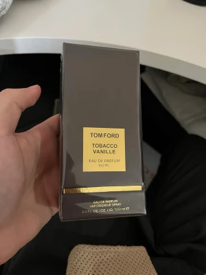 Tom Ford Tobacco Vanille Eau de Parfum oöppnad  - Tom Ford Tobacco Vanille Eau de Parfum 100 ml. Lyxig parfym i en elegant mörkbrun rektangulär kartong med guldfärgade detaljer och en gul etikett. Perfekt för dig som gillar exklusiva och djupa dofter med inslag av vanilj och tobak.