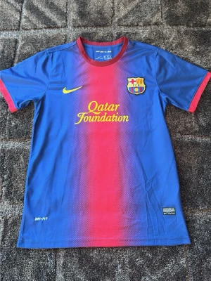Blå-röd FC Barcelona matchtröja Nike - Säljer en FC Barcelona matchtröja från Nike med Qatar Foundation och UNICEF-tryck. Tröjan är blå med röd gradient i mitten, har klubbemblem på bröstet och Dri-FIT material som håller dig sval. Perfekt för fotboll eller att visa support för laget.