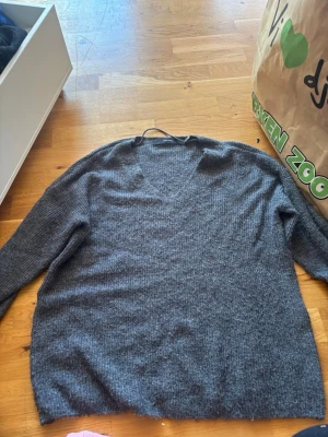 Grå stickad tröja Vero Moda - Mysig grå stickad tröja från Vero Moda med v-ringning och långa ärmar. Perfekt för lager-på-lager och enkel att matcha med jeans eller kjol. Tröjan är i mjukt material och har en klassisk, avslappnad passform.