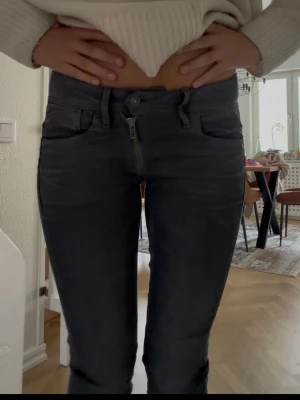 Mörkgrå bootcut jeans - Säljer ett par mörkgrå bootcut jeans med klassiska femficksdetaljer och snygga sömmar på bakfickorna. Jeansen har en låg midja och dragkedja framtill. Perfekta för dig som gillar en stilren och modern look.