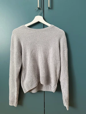 Stickad tröja - Mysig ljusgrå stickad tröja med rund halsringning och avslappnad passform. Tröjan har ribbstickade muddar vid ärmslut och nederkant samt långa ärmar. Perfekt för lager på lager och enkel att matcha med olika outfits.