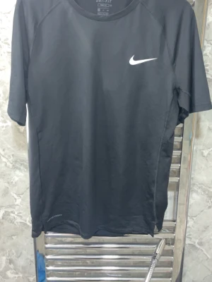 Svart Nike Pro träningströja - Svart kortärmad träningströja från Nike Pro med vit logga på bröstet. Tillverkad i ett lätt och snabbtorkande material som passar perfekt för intensiva träningspass. Tröjan har rund halsringning och en sportig passform.