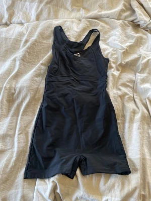 Svart baddräkt med ben från Speedo - Sportig svart baddräkt från Speedo med ben och brottarrygg. Framsidan har en diskret logga och baddräkten har en öppen rygg med vit insida. Aldeog använd