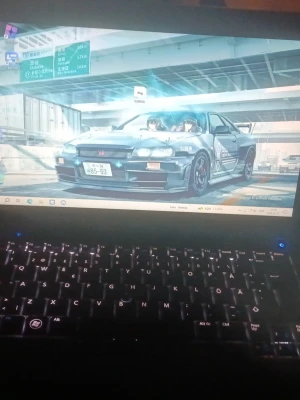 Svart bärbar dator med bakgrundsbelyst tangentbord - Säljer en svart bärbar dator med bakgrundsbelyst tangentbord. Skärmen visar en anime-inspirerad bakgrundsbild med en bil. Tangentbordet har tydliga vita tecken och datorn har en modern design med slimmad form.