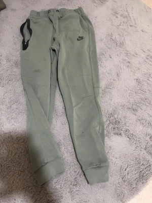 Gröna mjukisbyxor från Nike - Snygga gröna mjukisbyxor från Nike med resår i midjan och muddar vid bensluten. Byxorna har sidofickor och en liten Nike-logga broderad på vänster lår. Perfekta för chill eller träning, riktigt sköna och stilrena.har ett hål vid fickan men man kan sy enkelt 