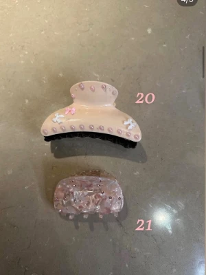 Två hårklämmor i rosa och beige med pärlor - Säljer två hårklämmor: en större beige/rosa klämma dekorerad med rosa pärlor, små blommor och en rosett, och en mindre klämma i rosa som är marmorerad.  1 för 70 2 för 110