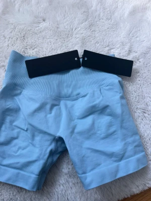 Ljusblå aura seamless scrunch shorts från Relode - Säljer ett par ljusblå seamless shorts från Relode med hög midja och ribbad kant. Shortsen har en scrunch-detalj bak och är tillverkade i ett stretchigt material som passar perfekt till träning eller chill. Supersnygg passform och trendig färg! Helt oanvända med prislappen kvar!