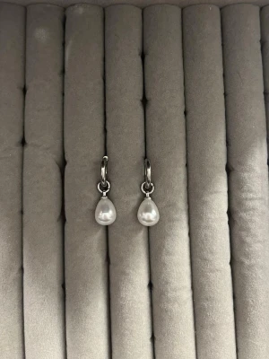 Silverörhängen med droppformade pärlor - Snygga örhängen i silverfärg med droppformade vita pärlor. Klassisk design med små ringar och hängande pärlor som ger en elegant touch till din stil. Perfekta för dig som gillar stilrena accessoarer.