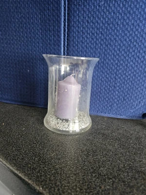 Ljuslykta med lila ljus - Säljer en stilren ljuslykta i klart glas med en lila cylinderformad ljus inuti. I botten finns dekorativa små grå stenar som ger en snygg kontrast. Perfekt som dekoration i hemmet för mysig stämning.