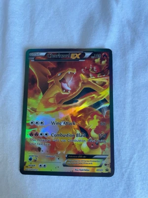 Charizard EX Pokémonkort - Säljer ett Charizard EX samlarkort från Pokémon TCG med holografisk yta. Kortet har färger i orange, gul och röd med en mäktig bild av Charizard. Perfekt för dig som samlar eller spelar Pokémonkort.