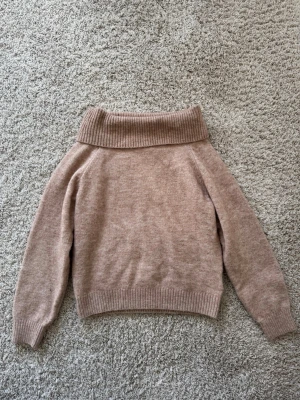 Beige stickad polotröja - Mysig beige stickad tröja som är off shoulder och långa ärmar. Tröjan har ribbstickade muddar vid ärmslut och nederkant, vilket ger en snygg och avslappnad look. Perfekt för kyliga dagar och enkel att matcha med olika outfits.