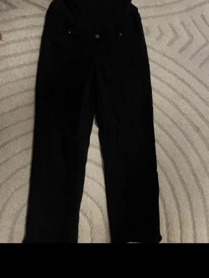Svarta raka jeans - Säljer ett par svarta gravid jeans med rak passform. Jeansen har knapp- och dragkedjestängning framtill och är perfekta för en stilren look. Materialet är denim och färgen är helsvart. Sömen har gått upp men inget som stör eller syns, går att sy ihop lätt 