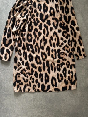 Leopardmönstrad kort klänning - Säljer en kort klänning med leopardmönster i beige och svart. Klänningen har långa ärmar och lätt puff vid axlarna för en trendig look. Materialet känns mjukt och stretchigt, perfekt för dig som vill sticka ut.