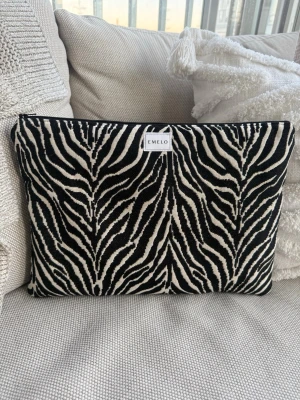 Laptop fodral  - Snygg datorväska från Emelo med zebra-mönster i svart och beige. Väskan har en mjuk textil utsida och stängs med dragkedja i svart. Perfekt för att skydda din laptop med stil och unik design. Passar laptop med maxmått 32x23 cm bäst 🌸