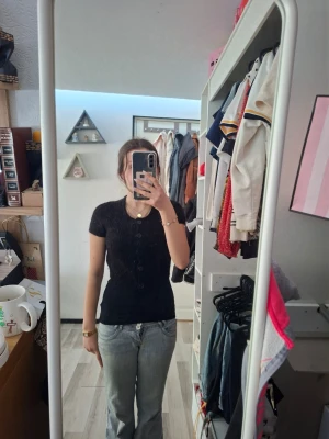 Svart croppad stickad blus med knappar - Säljer en fin svart blus med korta ärmar och knäppning framtill. Toppen är croppad och ger en trendig look. Perfekt för dig som gillar en stilren men ändå edgy vibe. Obs inte linnet under är inte med men är väldigt fin med ett linne under. Använd ändast nån gång.