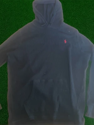 Marinblå hoodie från Polo Ralph Lauren - Snygg marinblå hoodie från Polo Ralph Lauren med klassisk huva och känguruficka framtill. Ikoniska röda loggan broderad på bröstet. Tillverkad i mjukt bomullsmaterial som är perfekt för chill dagar. Enkel och stilren design som funkar till det mesta.