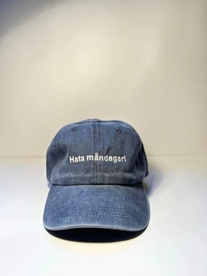 Keps ”hata måndagar” BLÅ - Den där känslan när väckarklockan ringer och själen lämnar kroppen. “Hata måndagar” är kepsen för dig som inte ens låtsas gilla starten på veckan.  Tillverkad i 100% ekologisk bomull så du åtminstone har det skönt när resten suger.