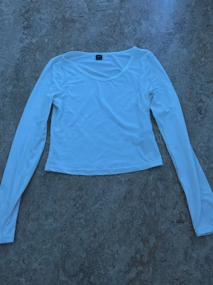 Vit långärmad topp  - En enkel och stilren vit långärmad topp Modellen är croppad med rund halsringning och har en slim passform. Perfekt att matcha med jeans eller kjol för en clean look.