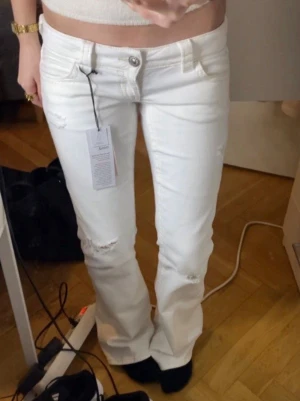 Vita bootcut jeans från Gina - Säljer ett par vita bootcut jeans från Gina Tricot Young som knappt är använda dock så har de några små fläckar som sannolikheten gör bort i tvätten. Jeansen är JÄTTE låga! De är lite långa på mig som är cirka 163cm, skulle rekommendera de för någon som är cirka 165