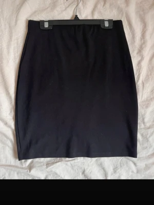 Svart enkel kortkjol i bomull - Säljer en svart, stilren och tight kortkjol i bomull. Kjolen har en klassisk rak form och passar perfekt till olika outfits. Inga synliga detaljer eller mönster, bara en clean look som är lätt att matcha.