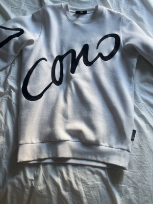 Vit sweatshirt med svart tryck - Cool vit sweatshirt  med stort svart tryck som sträcker sig över bröstet och ena ärmen. Tröjan har rund halsringning, ribbade muddar och är gjord i mjukt bomullsmaterial. Perfekt för dig som gillar streetstyle och grafiska prints. Lite nopprig 