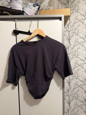 Grå tröja från Gina Tricot - En enkel och stilren grå tröja från Gina Tricot i storlek XS. Tröjan har korta ärmar, rund halsringning och är gjord i mjukt bomullsliknande material. Perfekt att matcha med jeans eller kjol för en clean look.