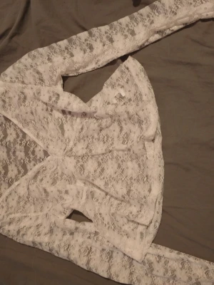 Vit spetsblus med omlott - Säljer en superfin vit blus i spets med omlottdesign. Blusen är genomskinlig, har långa ärmar och ett romantiskt uttryck. Perfekt att styla med ett linne under eller till höga jeans. Fräsch och trendig look!