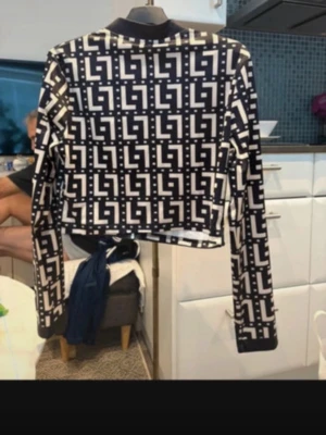 Svartvit bomberjacka med grafiskt mönster - Säljer en svartvit bomberjacka med grafiskt rutigt mönster och dragkedja framtill. Jackan har lång ärm, croppad passform och ribbade muddar vid hals och ärmslut. Materialet känns som polyester eller syntet och jackan har en modern, edgy vibe.