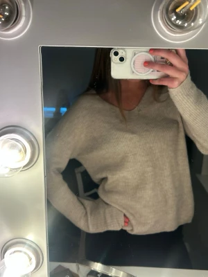 Beige stickad tröja från ONLY - Mysig beige stickad tröja från ONLY med v-ringning och långa ärmar. Tröjan har en avslappnad passform och är ribbstickad för extra struktur. Perfekt att slänga på sig när det är kyligt ute.