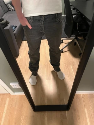 Gråa Jeans - Säljer ett par grå jeans från Jack and Jones med rak passform och klassisk femficksdesign. Jeansen har en snygg tvättad look och är tillverkade i mjuk denim. Perfekta för dig som gillar en enkel och stilren stil.