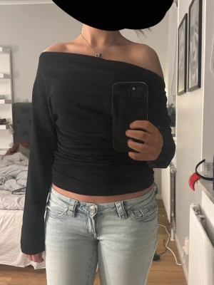 Svart offshoulder topp - Trendig svart offshoulder topp med lång ärm och croppad passform. Sitter snyggt och markerar axlarna, perfekt till jeans eller kjol. Mjuk och stretchig känsla för en bekväm look.