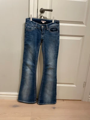 Bootcut jeans - Snygga blå bootcut jeans med broderade bakfickor med knappar. Klassisk femficksmodell i stretchigt denimtyg. Perfekta för dig som gillar en retroinspirerad look med extra detaljer på fickorna. De passar dig som är ca 165 cm