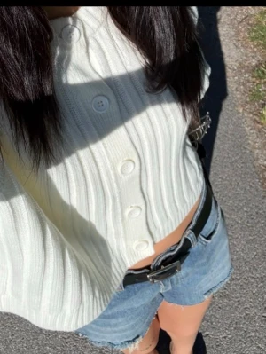 Vit ribbstickad kortärmad kofta - Säljer en söt vit ribbstickad kofta med korta ärmar och stora knappar framtill. Koftan är croppad och har rund halsringning. Perfekt att styla med jeans eller kjol för en fräsch look.