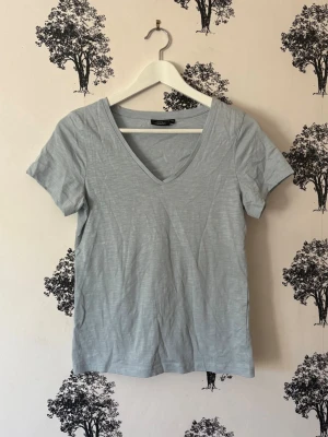 Ljusblå v-ringad t-shirt - Säljer en ljusblå t-shirt från Kappahl med v-ringning och korta ärmar. Tillverkad i mjuk bomull och har en enkel, clean design som passar perfekt till jeans eller shorts. Skön passform och lätt att matcha med olika stilar.