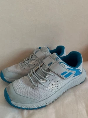 Blåa tennisskor - Snygga tennisskor från babolat i ljusblå med blå detaljer. Skorna har både snörning och kardborreband för enkel påtagning. Ovandelen är i mesh och syntetmaterial för bra andningsförmåga. Perfekta för en sportig look.