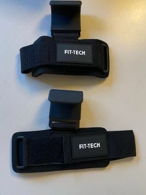 Svarta lyftkrokar från FIT-TECH - Säljer ett par svarta lyftkrokar från FIT-TECH. De har breda vadderade handledsband med kardborrestängning och kraftiga metallkrokar för extra grepp vid styrketräning. Nya! 