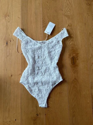Vit spetsbody från zara - Säljer en snygg vit body från zara i spetsmaterial. Bodyn har off shoulder-modell med smala axelband och v-ringning. ny med lappen kvar 