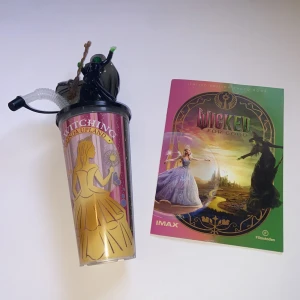 Wicked IMAX häfte + souvenirbägare - Säljer ett färgglatt IMAX-häfte från filmen Wicked samt en souvenirbägare med motiv från samma film. Häftet har glansigt omslag med illustrationer av huvudkaraktärerna och bägaren är dekorerad med en gul klänning och figurer på locket. Perfekt för samlare av filmprylar. Fick de när jag såg på wicked för good 💖💚. Kan inte köpas på annat ställe. Har druckit ur bägaren men den är diskad. 🫧🫧🫧